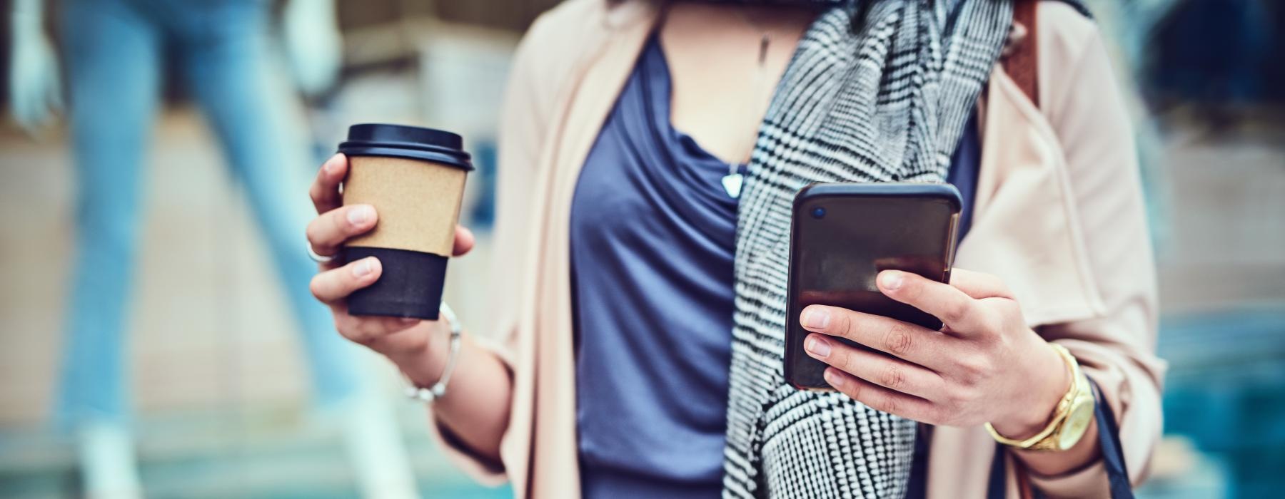 woman with a shopping bag and coffee cup walks with a cell phone